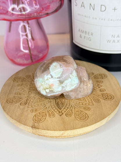 Pink and white flower agate skull on a wooden coaster in front of a black candle jar and pink vase