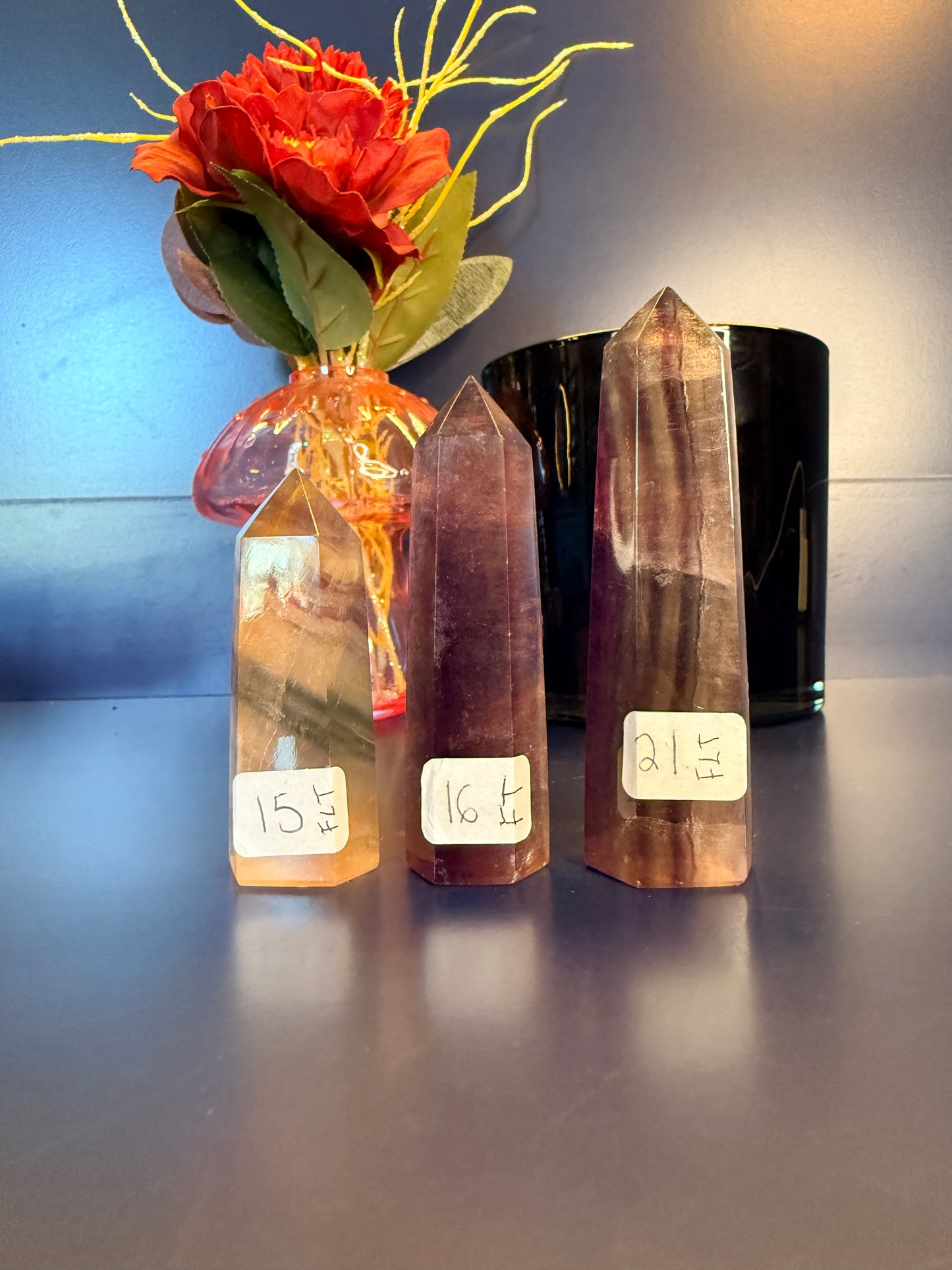 Three fluorite towers with labels on a reflective surface next to a decorative flower.