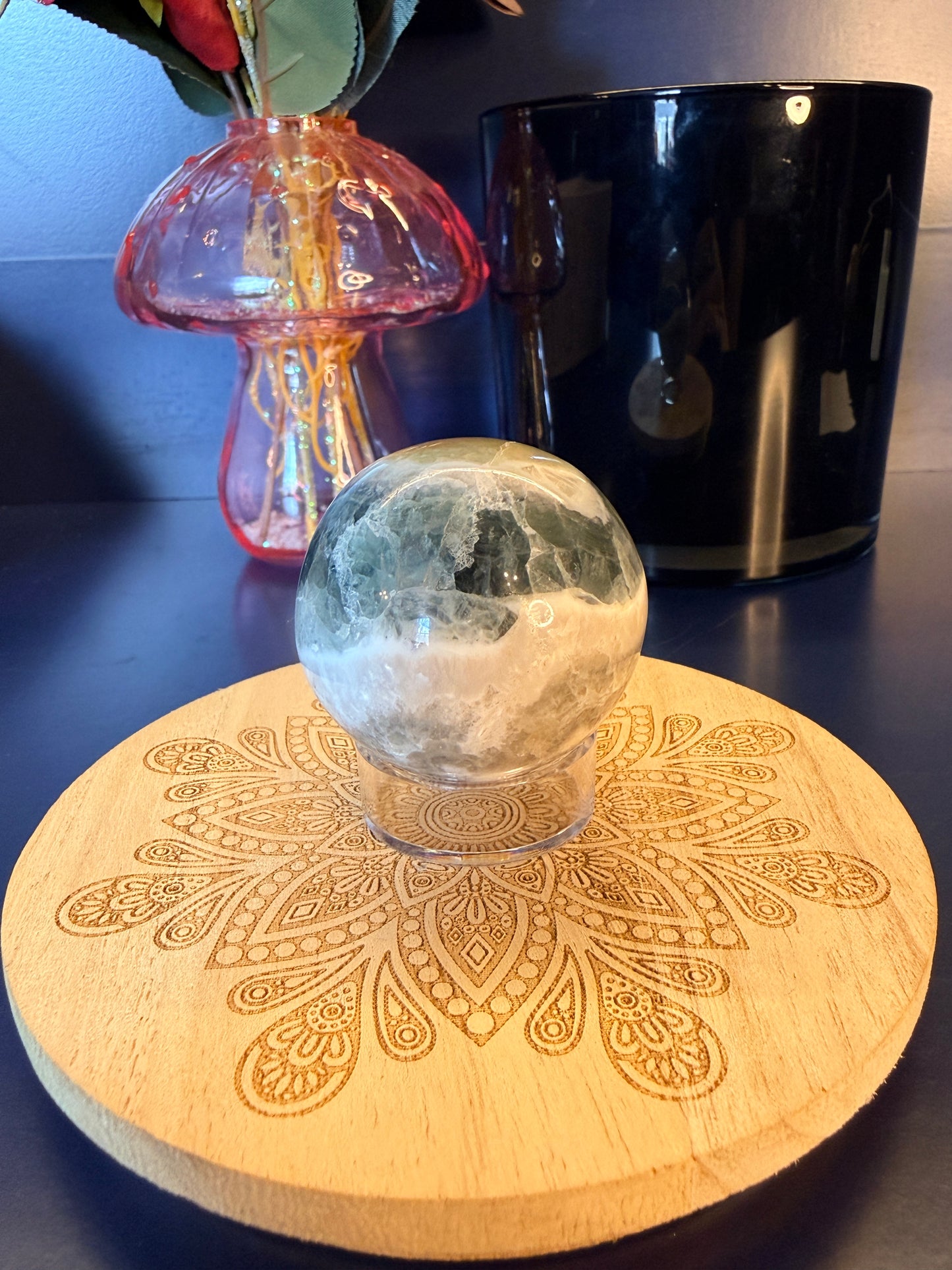 White and green crystal sphere sitting on a decorative coaster in front of a mushroom vase and black jar