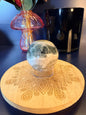 White and green crystal sphere sitting on a decorative coaster in front of a mushroom vase and black jar