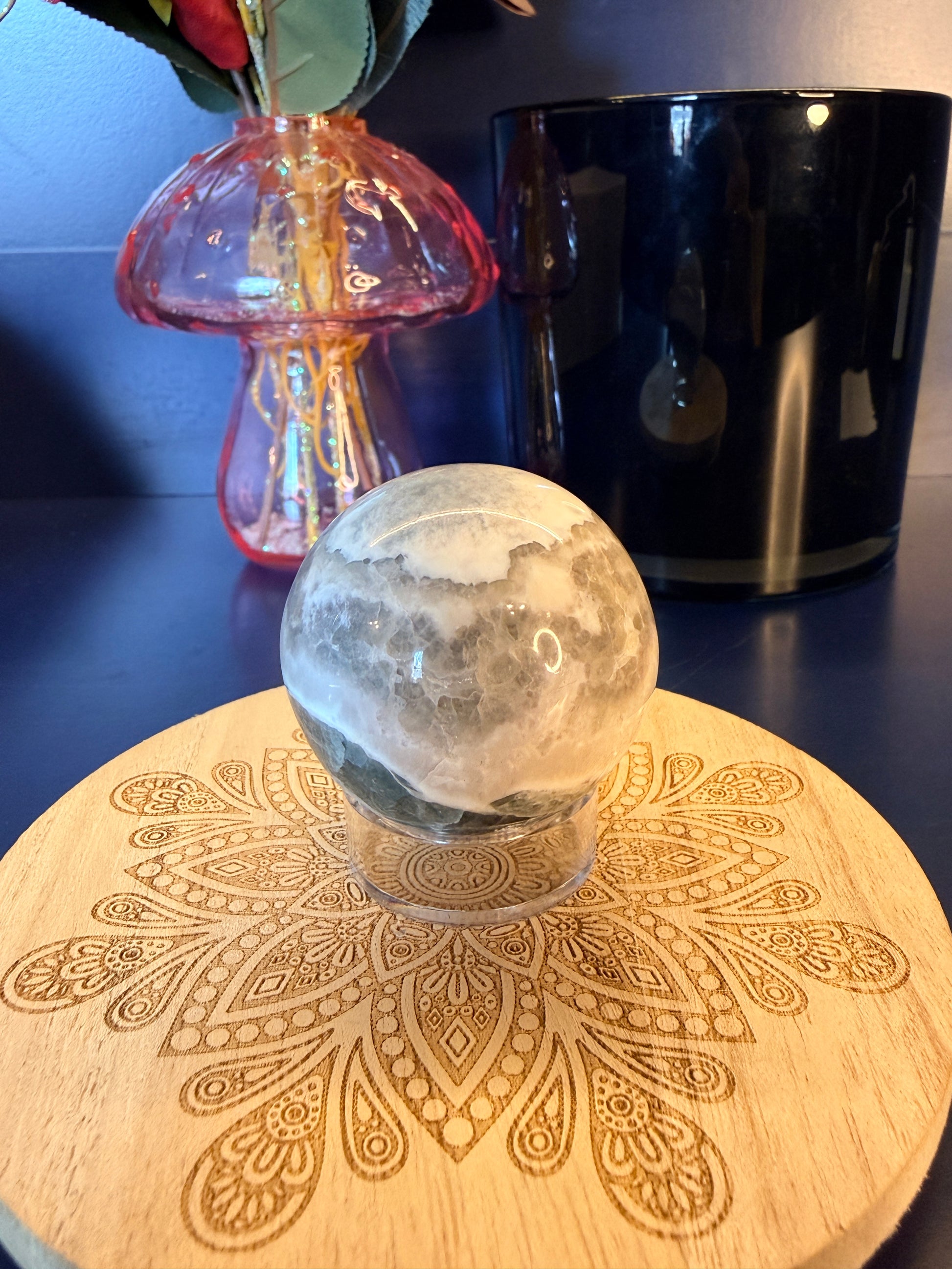 White and green crystal sphere sitting on a decorative coaster in front of a mushroom vase and black jar