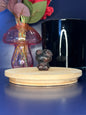 Red and black crystal kitty carving in front of a pink vase and black jar on a wooden coaster against a blue background