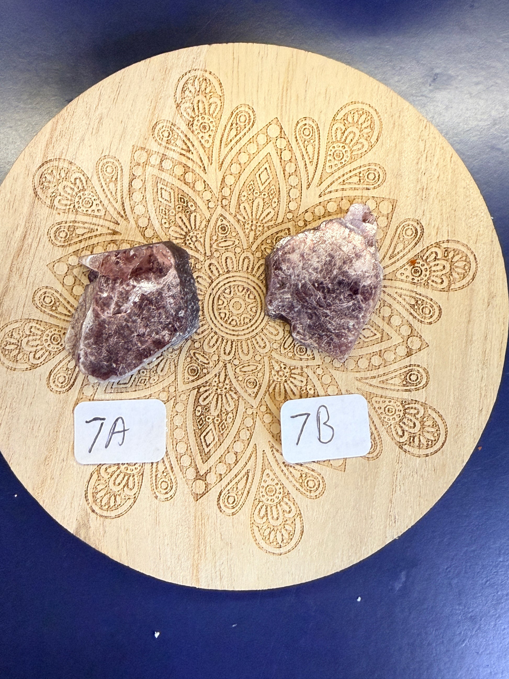Two purple lepidolite pieces on a decorative wooden coaster on a blue background
