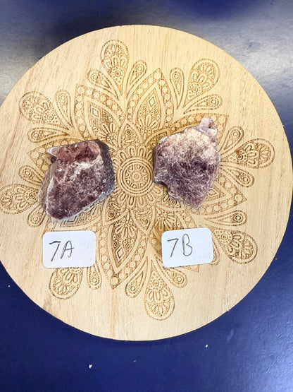 Two purple lepidolite pieces on a decorative wooden coaster on a blue background
