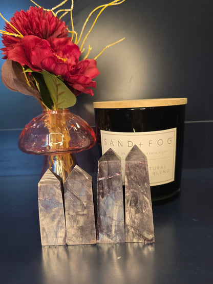 Four bright purple gem lepidolite towers in front of a red flower in a vase and a black candle jar