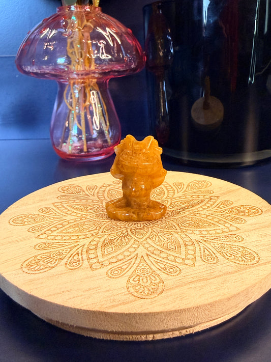 A golden healer quartz meowth crystal sitting on a decorative wooden coaster in front of a glass mushroom and black jar