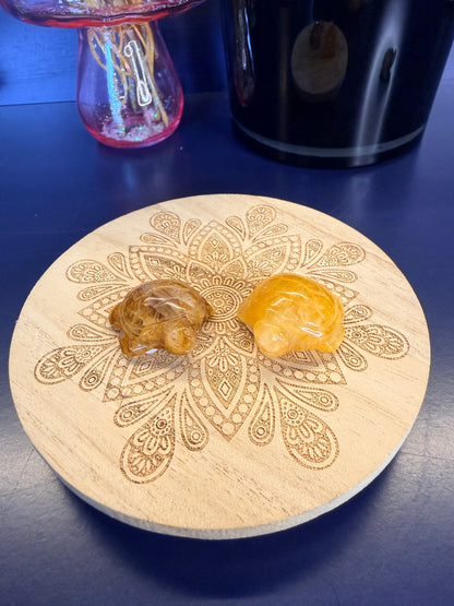 Two yellow crystal turtles on a decorative wooden coaster in front of a vase and black jar