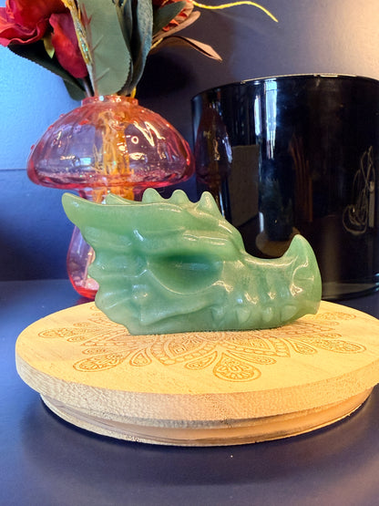A large green aventurine dragon head sitting on a decorative wooden coaster in front of a glass mushroom and black jar