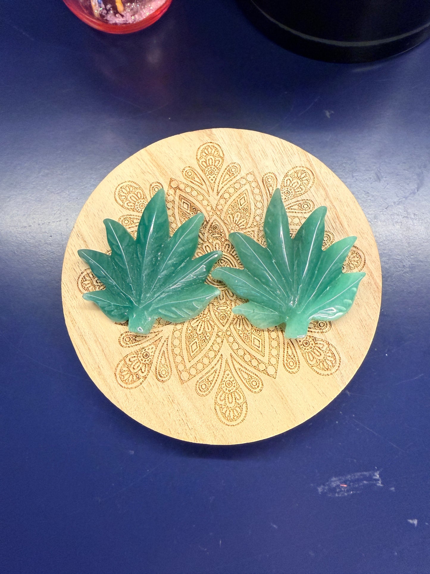 Two green aventurine leaves on a decorative wooden coaster against a blue background
