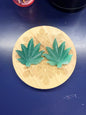Two green aventurine leaves on a decorative wooden coaster against a blue background