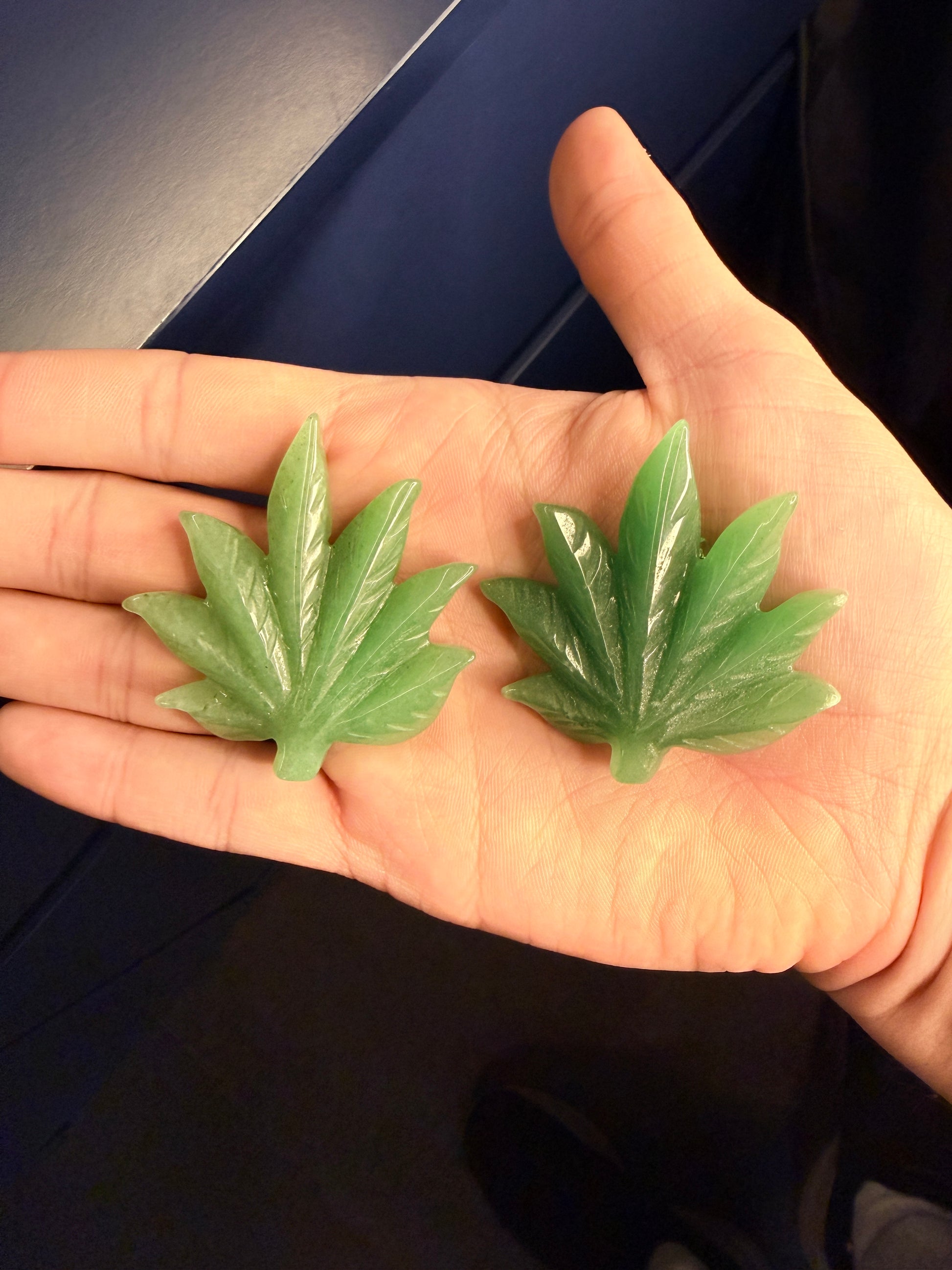 Hand holding two green aventurine leaves against a dark background