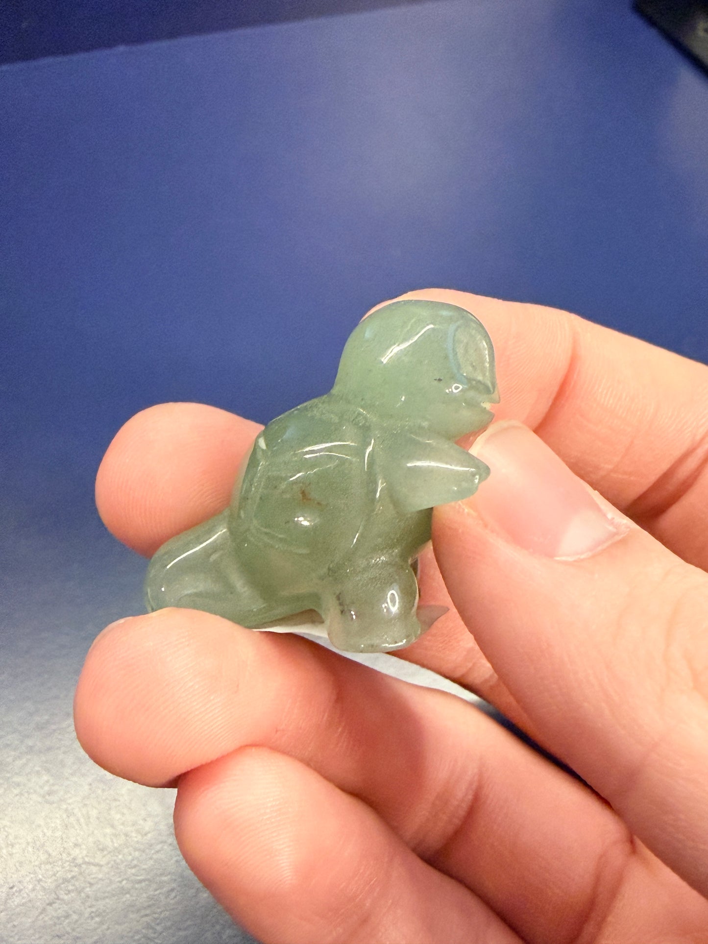 Hand holding a green aventurine squirtle on the side against a blue background