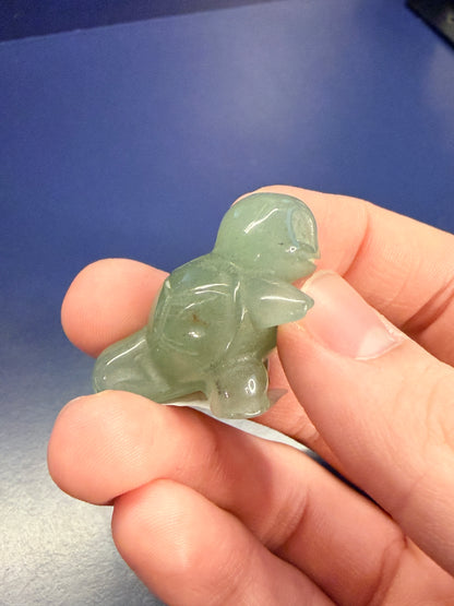 Hand holding a green aventurine squirtle on the side against a blue background