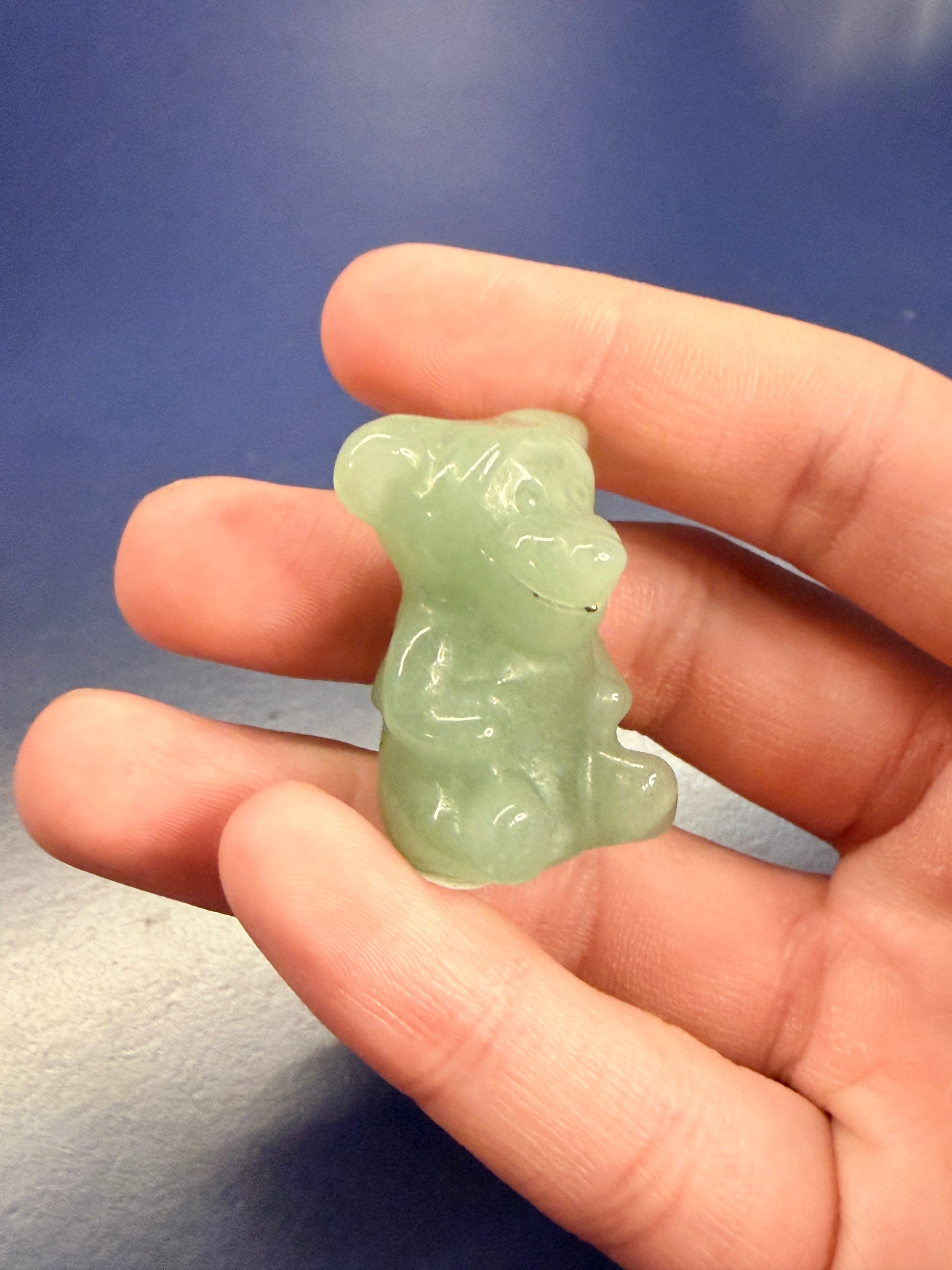 Hand holding a green aventurine tigger crystal against a blue background