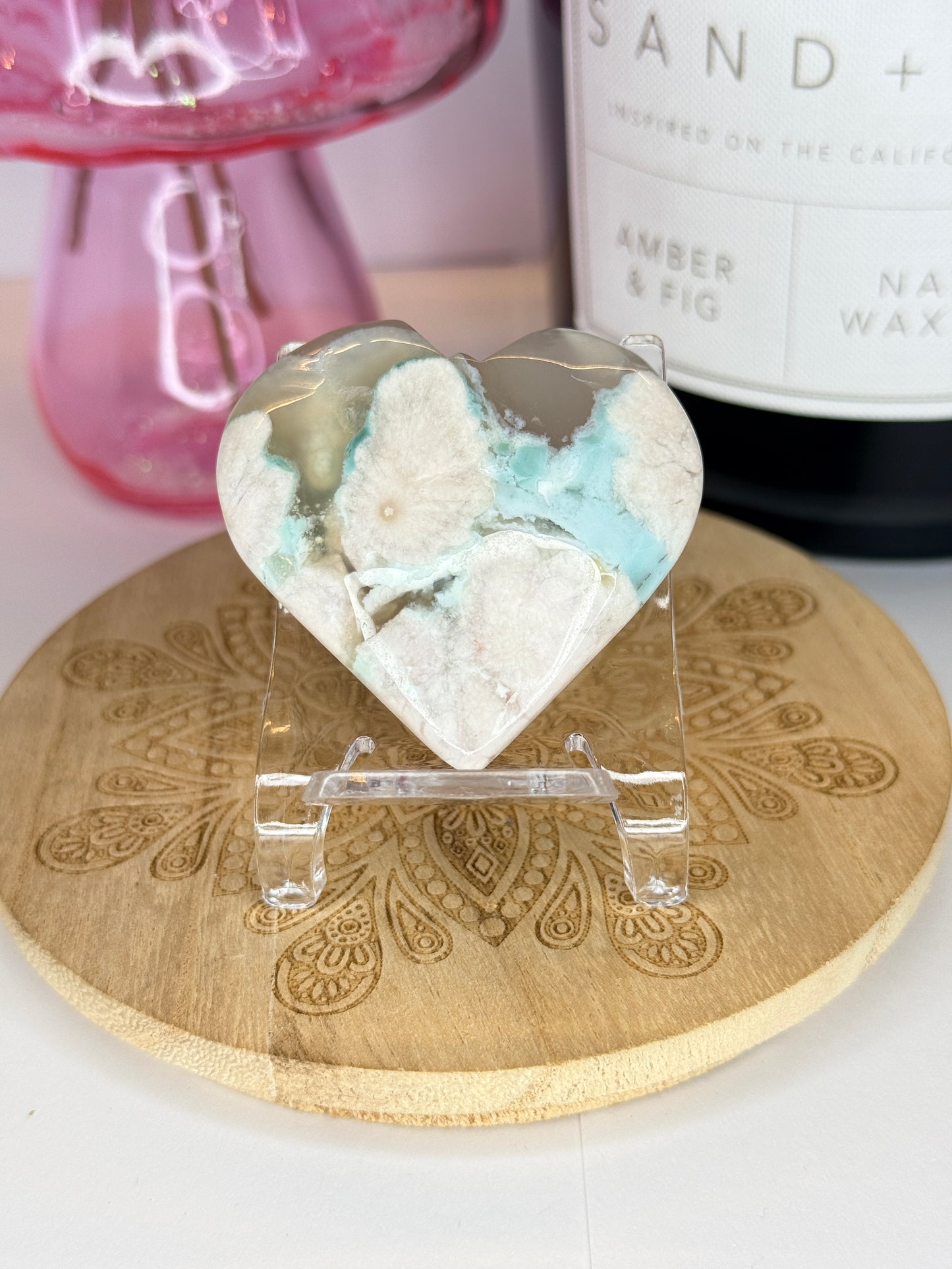 White and green flower agate heart on a wooden coaster in front of a black candle jar and pink vase