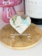 White and green flower agate heart on a wooden coaster in front of a black candle jar and pink vase