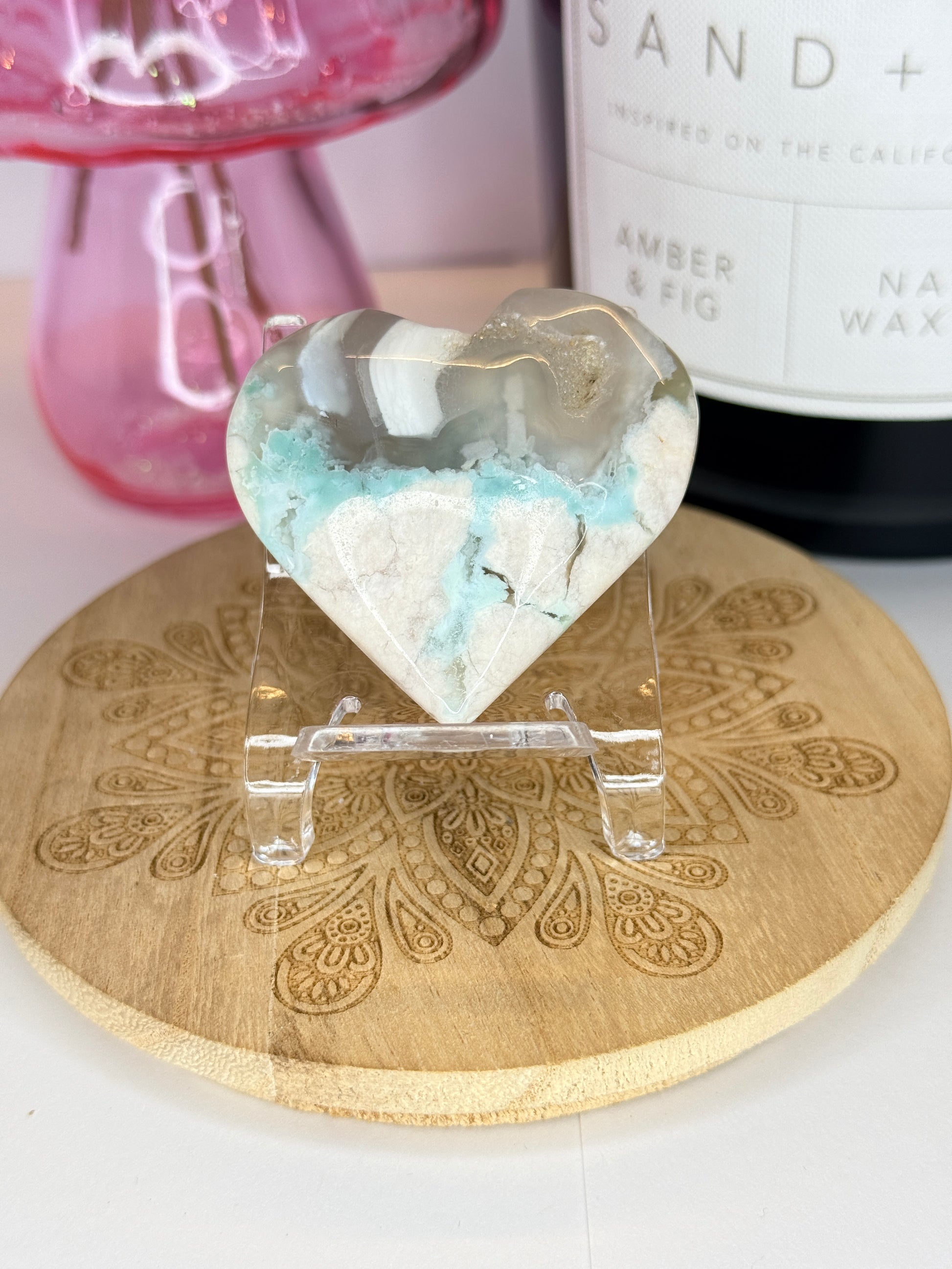 White and green flower agate heart on a wooden coaster in front of a black candle jar and pink vase