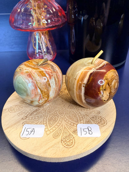 Two brown, red, and green onyx apples on a decorative wooden coaster in front of a mushroom vase and black jar
