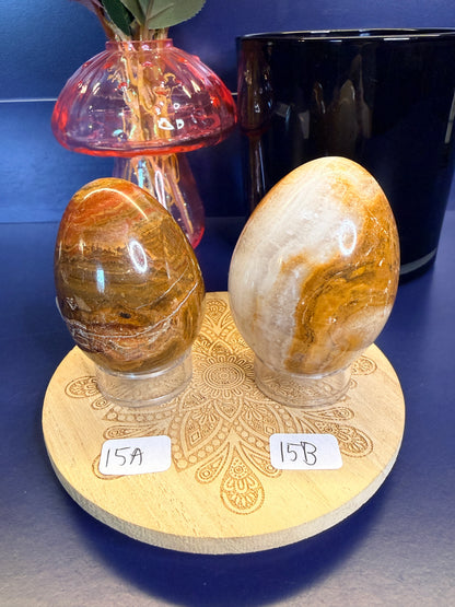 Two brown, red, and green onyx eggs on a decorative wooden coaster in front of a mushroom vase and black jar