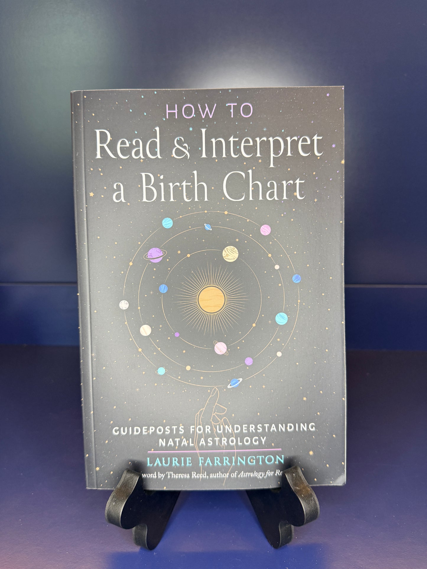 Book titled 'How to Read & Interpret a Birth Chart' by Laurie Farrington on a stand against a dark background