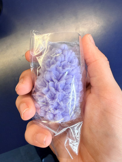 Hand holding a purple floral soap bar on a blue background