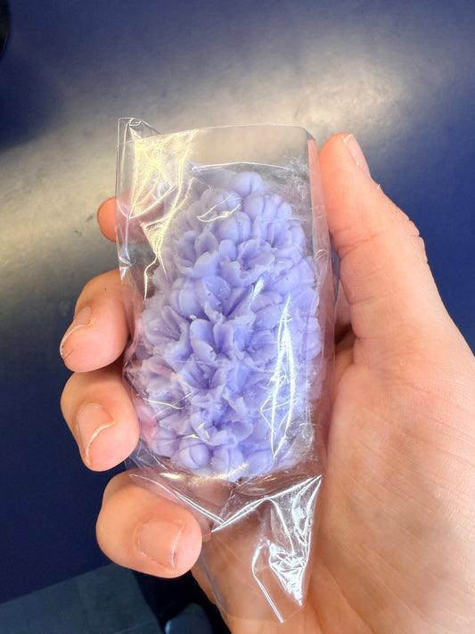 Hand holding a purple floral soap bar on a blue background