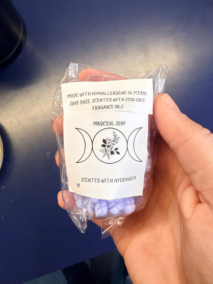 Hand holding a purple floral soap bar with two labels on a blue background