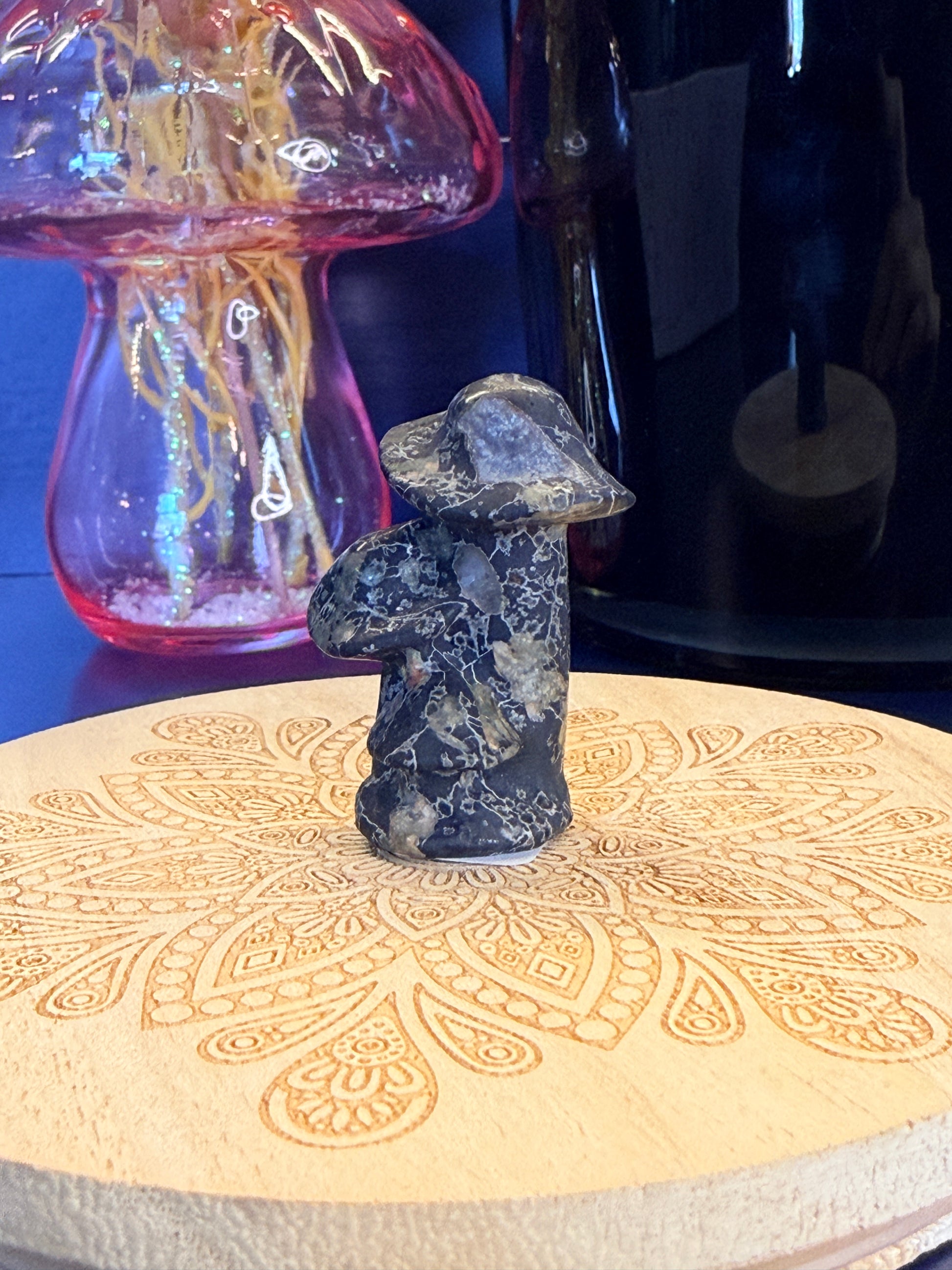 A blue patterned crystal mushroom in front of a mushroom vase and black jar