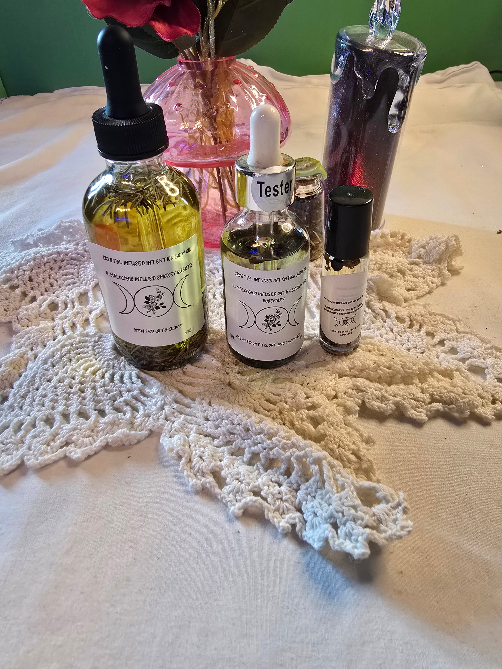 Three glass bottles filled with clear and yellow body oil with herbs on a white crochet mat and white table cloth