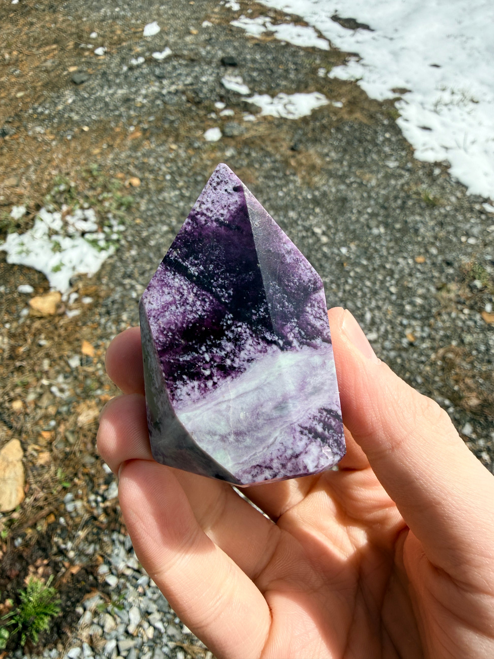 Hand holding a dark purple kammererite freeform in front of gravel