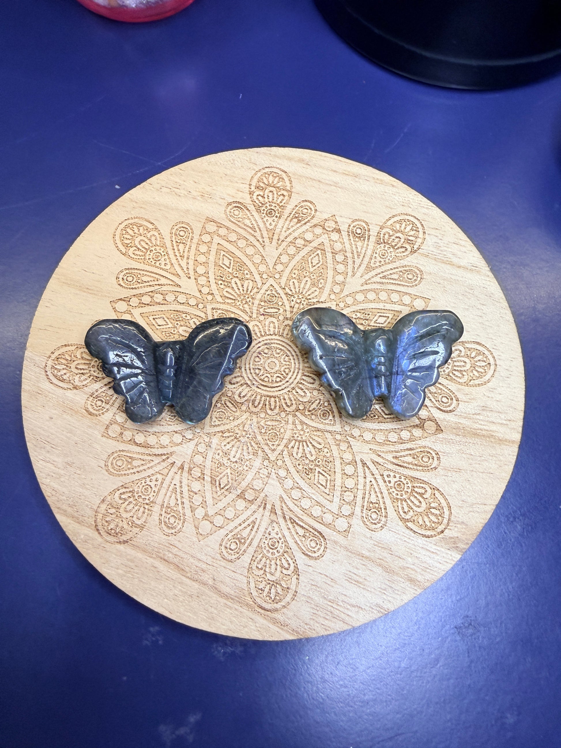 Two labradorite butterflies sitting on a decorative wooden coaster against a blue background