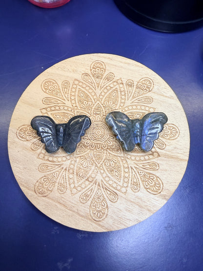 Two labradorite butterflies sitting on a decorative wooden coaster against a blue background