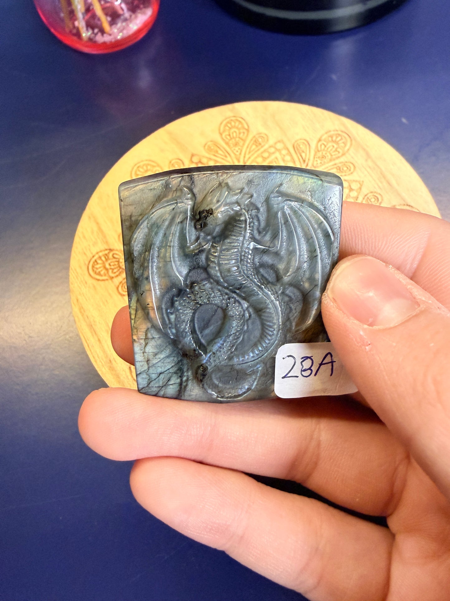 Hand holding a labradorite dragon slab with a yellow flash in front of a wooden coaster against a blue background
