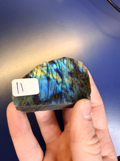 Hand holding a colorful labradorite stone with a label against a blue background