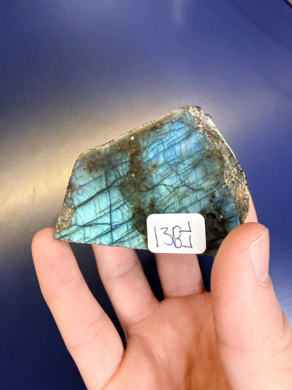 Hand holding a colorful labradorite stone with a label against a blue background