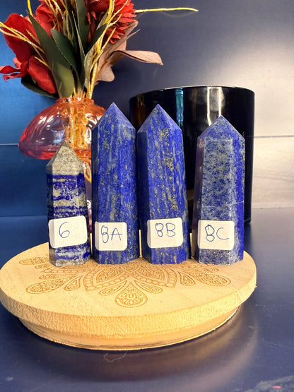 Four blue and grey lapis lazuli towers on a wooden coaster in front of a red flower and black jar