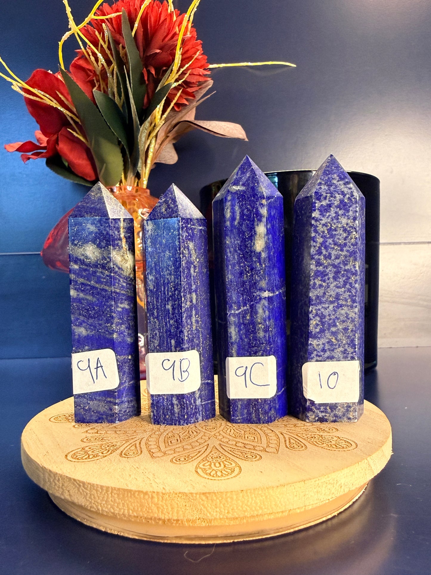 Four blue and grey lapis lazuli towers on a wooden coaster in front of a red flower and black jar