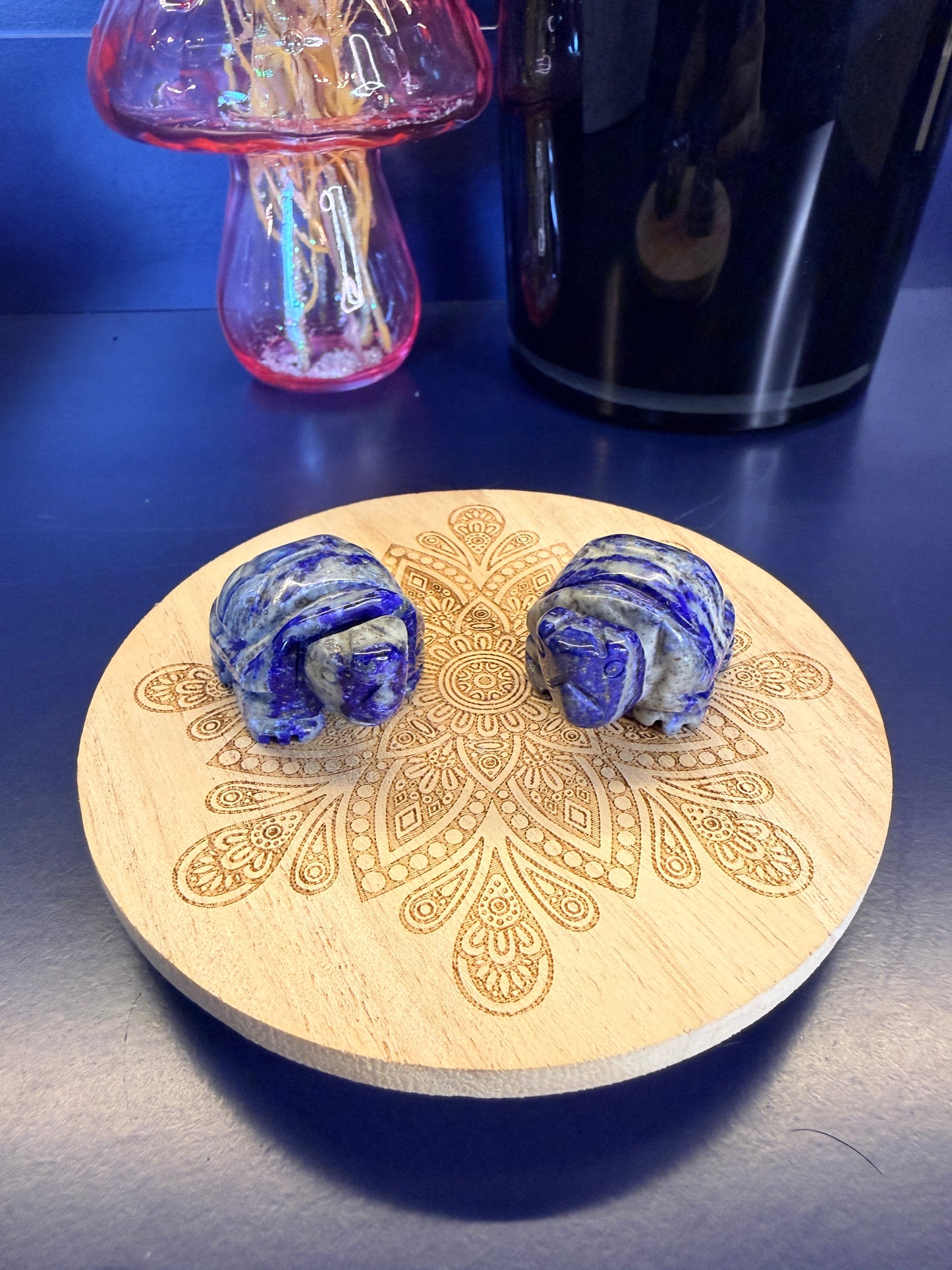 Two blue and grey crystal turtles on a decorative wooden coaster in front of a mushroom vase and black jar