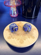 Two blue and grey crystal turtles on a decorative wooden coaster in front of a mushroom vase and black jar