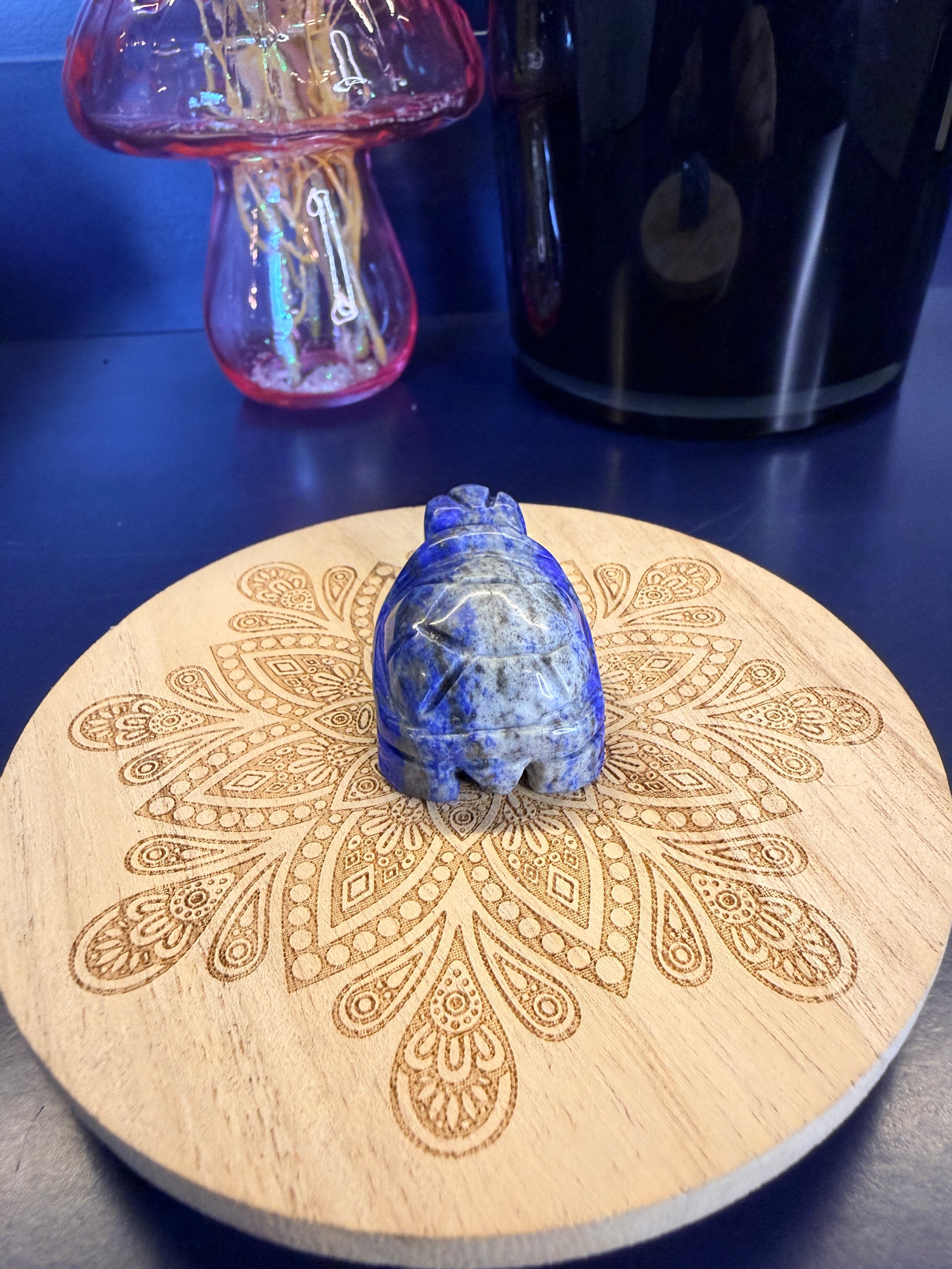 Blue and grey crystal turtles on a decorative wooden coaster in front of a mushroom vase and black jar