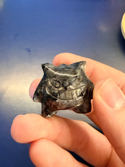 Hand holding a larvikite gengar-inspired crystal against a blue background