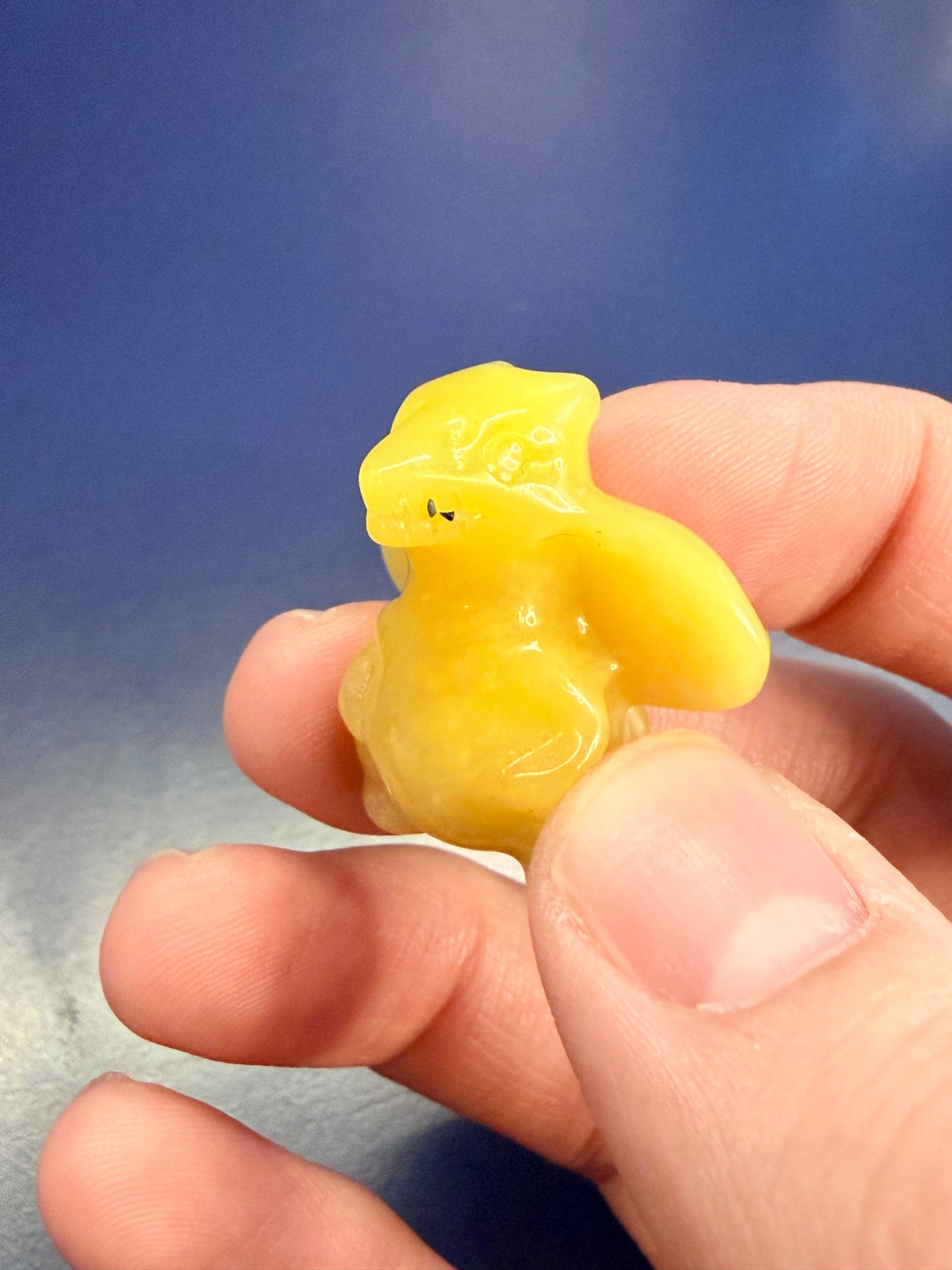 Hand holding a lemon calcite crystal carving of a charizard-inspired creature against a blue background