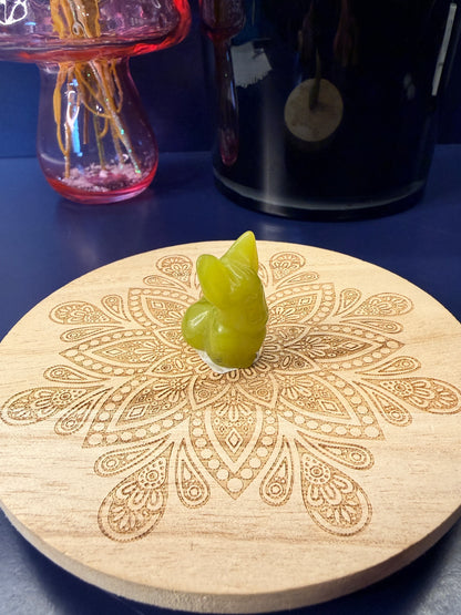 Lemon Calcite eevee crystal shape sitting on a decorative wooden coaster in front of a glass mushroom and black jar