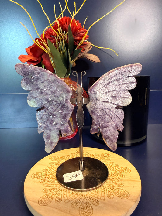 Two large purple lepidolite butterfly wings on a decorative wooden coaster in front of red flowers and black jar