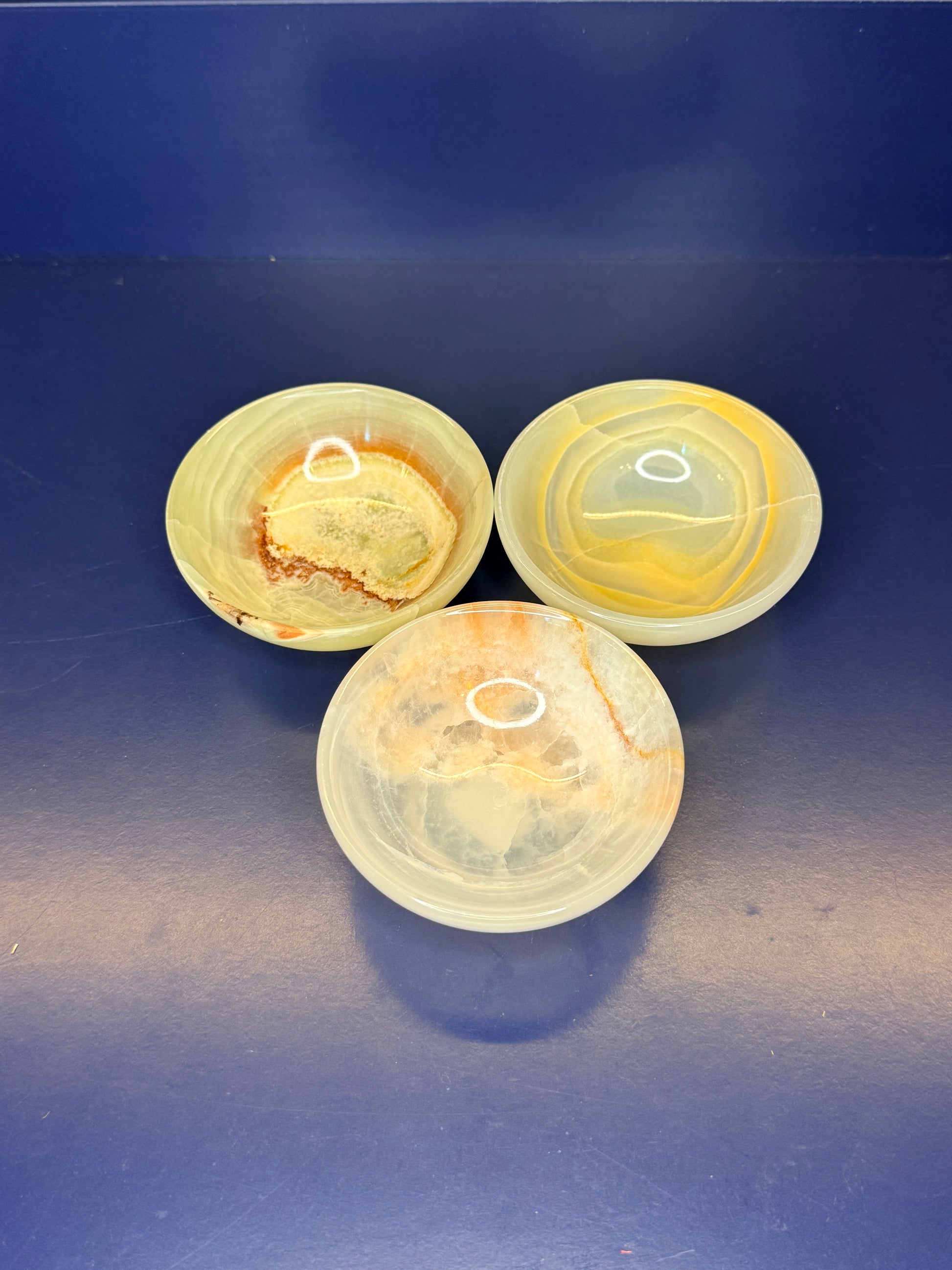 Three light green onyx bowls on a dark blue background