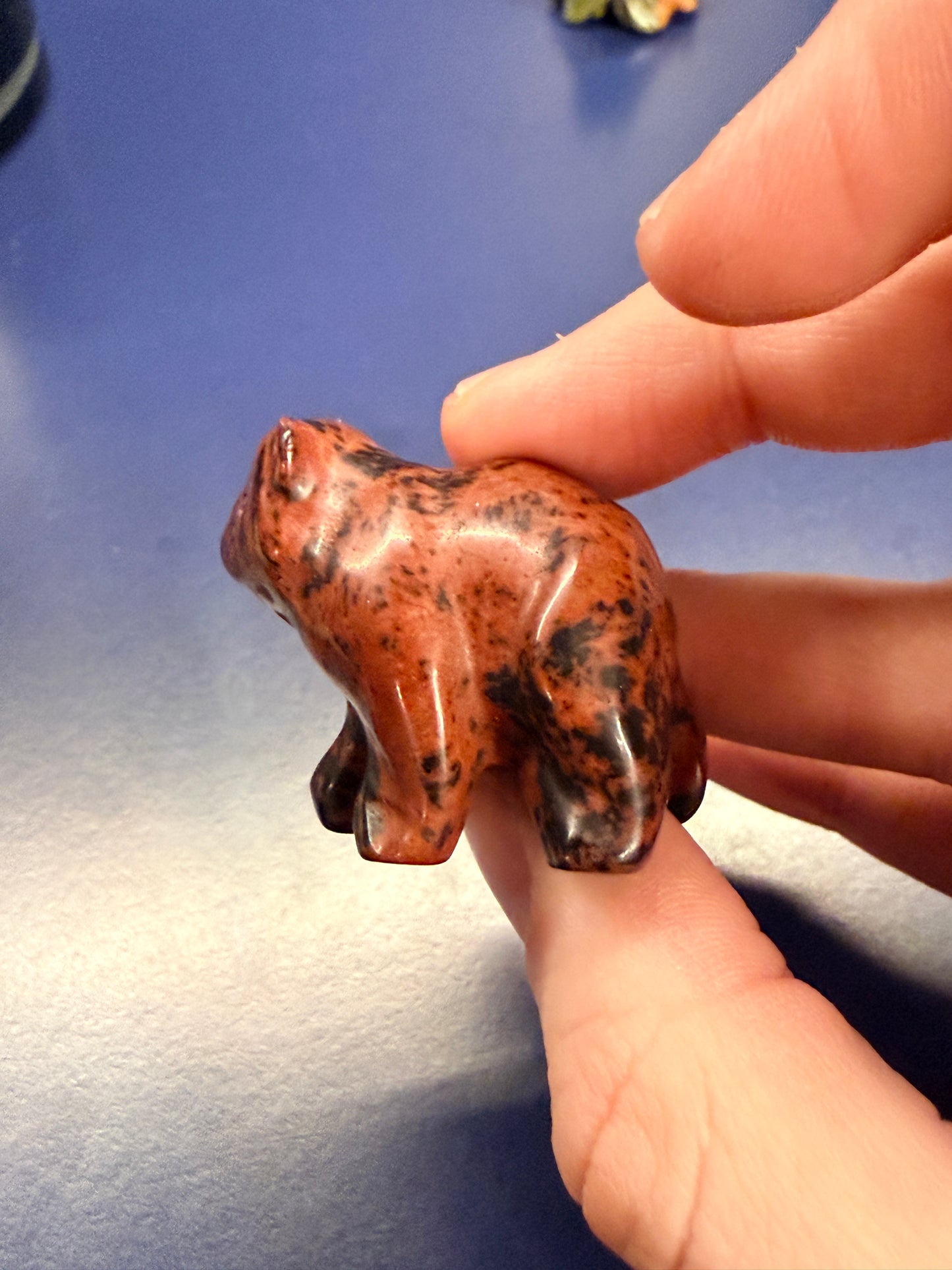Hand holding a mahogany obsidian bear crystal against a blue background