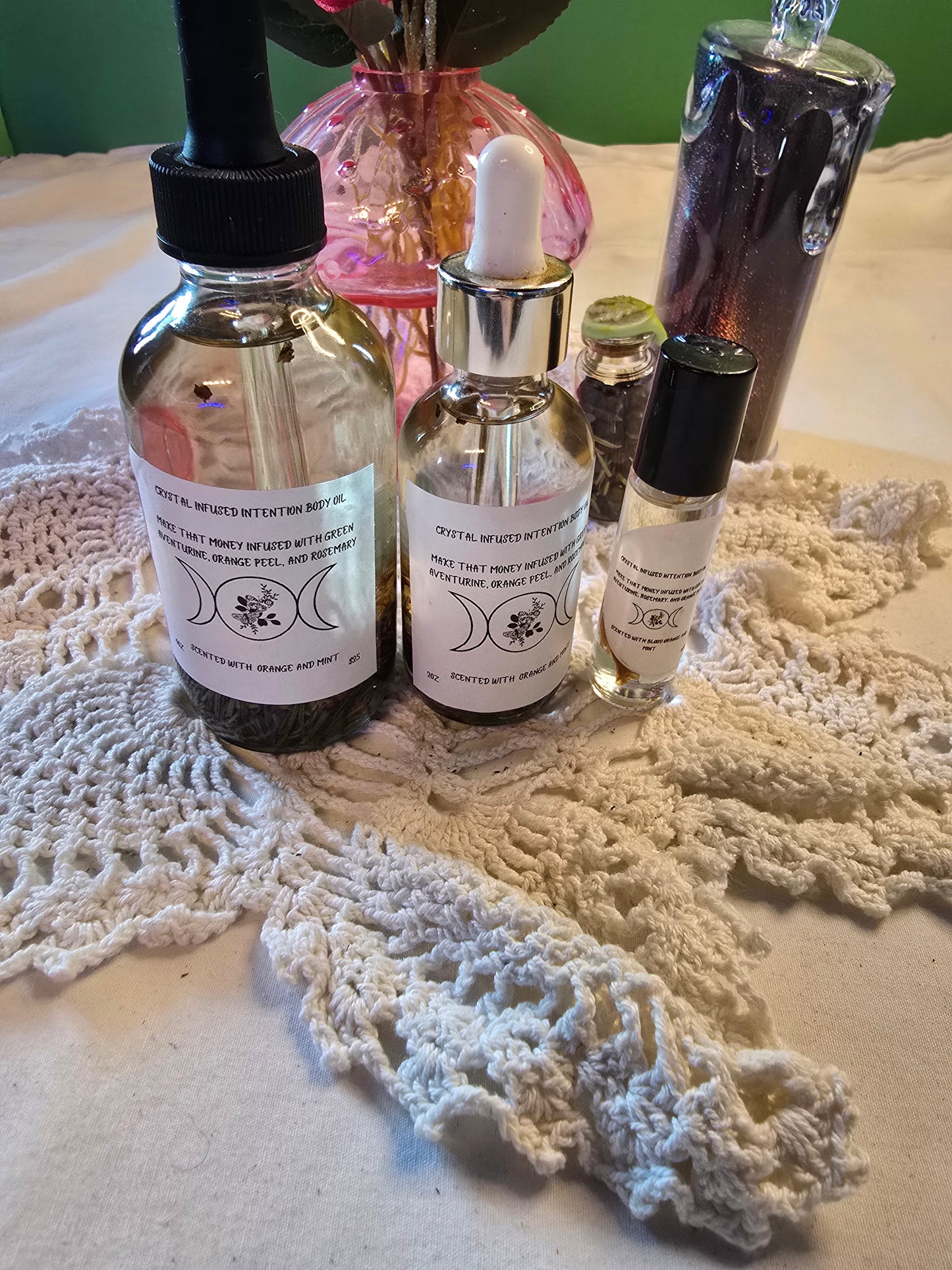 Three glass bottles filled with clear body oil with herbs on a white crochet mat and white table cloth