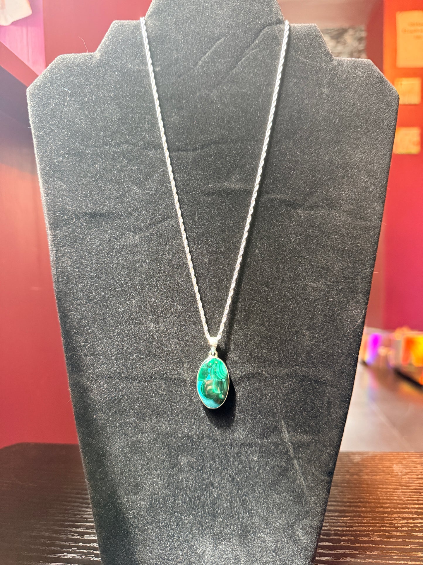 Sterling silver necklace resting on a black velvet jewelry stand holding a green and blue malachite and chrysocola pendant 