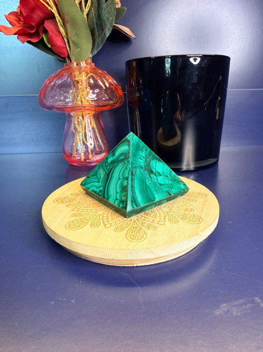 A green marbled malachite pyramid on a wooden coaster in front of a red flower in a vase and black jar