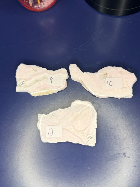 Three light pink and white mangano calcite slabs on a blue background
